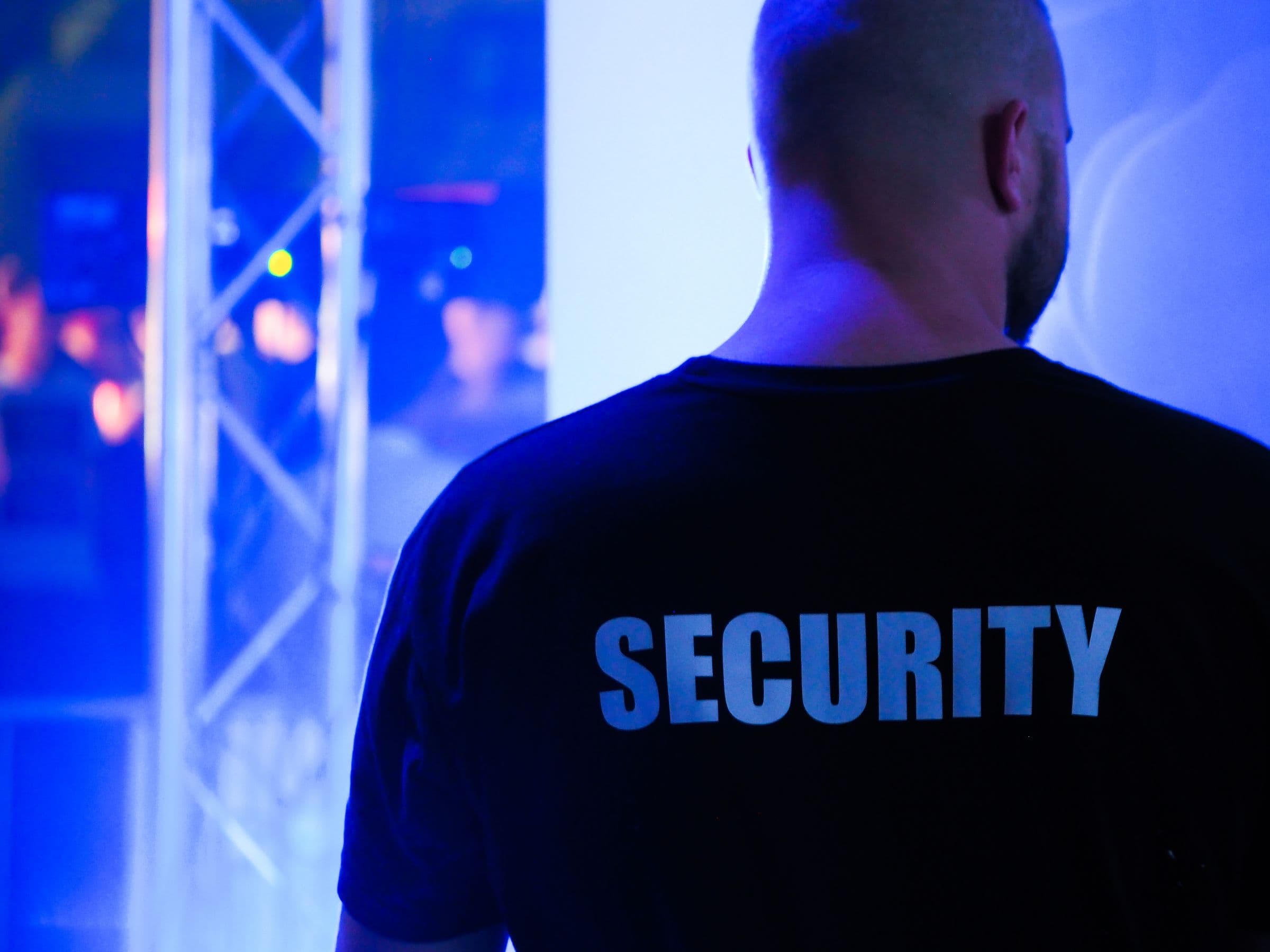 A door supervisor on duty at the edge of a lit venue floor.